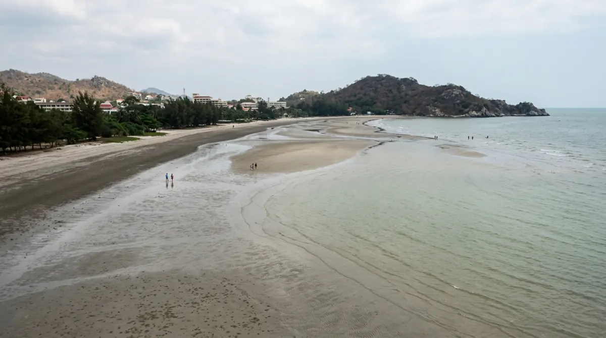 Wide firm beach at low tide with a rocky headland at one end